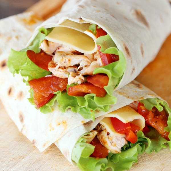 Two chicken fajita wraps with lettuce, tomatoes, and cheese on a wooden board.